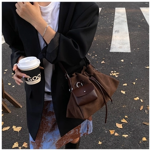 Outdoor shot of a brown suede bucket bag with leather drawstring and front pocket detail