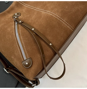 Detail of brown suede tote bag with white stitching and decorative metal zipper
