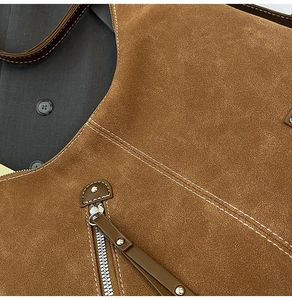 Detail of brown suede tote with white contrast stitching and silver zipper pull