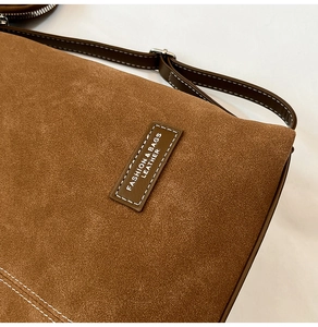 Detail of brown matte suede bag with contrast stitching and leather fashion label