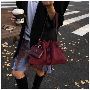 Deep red bucket bag with drawstring closure and small matching pouch in street setting