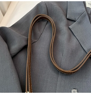 Detail of dark brown leather strap with white contrast stitching on grey blazer