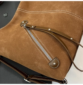 Detailed close-up of brown suede bag with silver zippers, rivets, and white contrast stitching