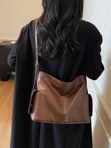 Brown leather shoulder bag with side pockets shown on model in minimal indoor setting