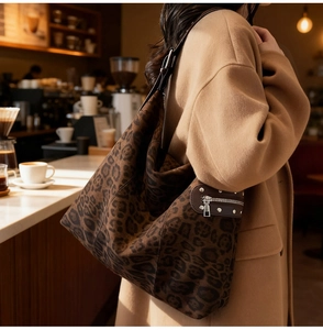 Macro shot of large leopard print suede shoulder bag with rivets in a warm cafe setting