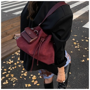 Detail of burgundy suede bucket bag with drawstring closure and mini pouch in autumn street