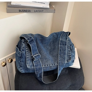 Dettaglio della borsa a tracolla grande in denim blu scuro su un cuscino nero testurizzato