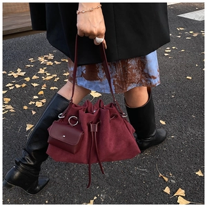 Detail of burgundy suede tote bag with drawstring closure and matching mini pouch in autumn scenery