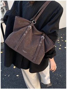 Detail of dark brown leather tote bag with embossed text worn by model in autumn setting
