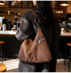 Detail view of brown suede hobo bag with metal rivets and wide strap in a cafe setting