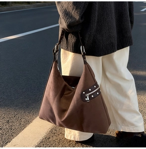 Close-up of brown suede shoulder bag with silver rivet details and adjustable strap