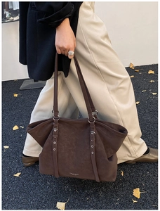 Macro shot of dark brown suede tote bag featuring metallic eyelets and long shoulder straps