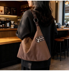 Detailed close-up of brown suede shoulder bag with silver studs and metal ring strap