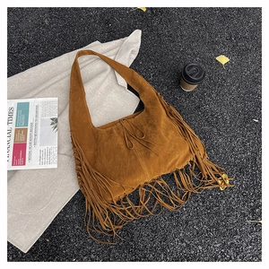 Detail view of brown suede tassel tote bag with long fringes on autumn leaf background