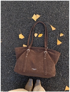 Macro shot of dark brown retro leather tote bag with silver ring buckles on ginkgo leaves