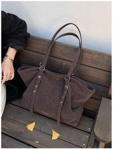 Dark brown matte tote bag with decorative straps on a vintage park bench with leaves