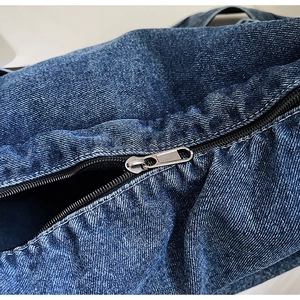 Dettaglio della trama denim blu scuro e della cerniera in metallo argentato della borsa