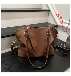 Detail of a brown suede tote bag with glossy leather handles and gold metal ring accents