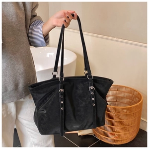 Detail of a black suede tote bag with long shoulder straps and silver buckle accents