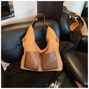 Nahaufnahme der braunen Wildleder-Hobo-Tasche mit Metallnieten auf schwarzem Sofa