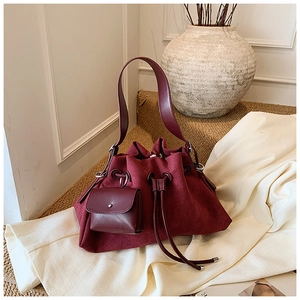Detail of burgundy drawstring bucket bag with matching mini square charm on a strap