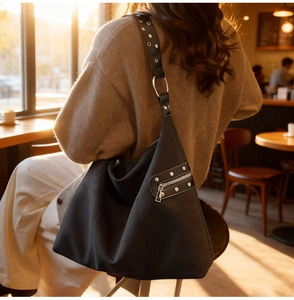 Detail of black suede hobo bag featuring silver rivets and stylish zipper pocket