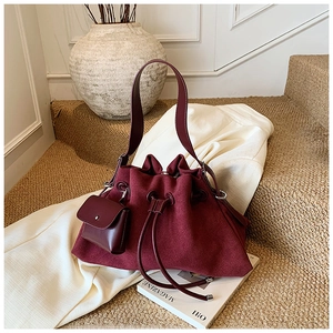 Detail of burgundy suede bucket bag featuring drawstring closure and matching mini pouch