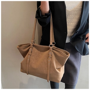 Close-up of camel tote bag with dual metal buckle straps and smooth leather texture