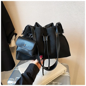 Detail of black matte bucket bag with small pouch resting on a silver suitcase