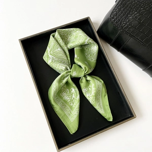 Détail d'un foulard en soie vert avec motif cachemire blanc sur plateau noir