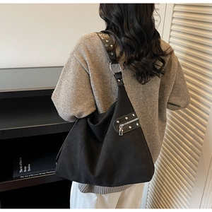 Detail of black tote bag featuring silver studs and metal zippers on a suede texture