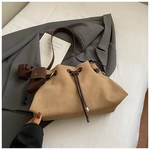 Detail of brown suede bucket bag with drawstring closure and mini pouch charm on strap