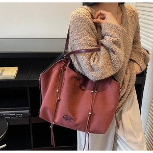 Détail du grand sac cabas bordeaux en daim avec pompons porté par un mannequin chic