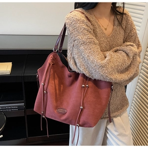 Détail du sac cabas en daim rouge brique avec boucle métallique et longue décoration de franges