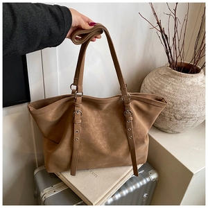 Detail of the brown leather tote bag showing handle attachments and metallic buckles