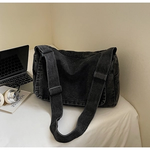Borsa a tracolla vintage in denim nero con tracolla regolabile accanto al laptop