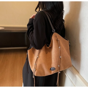 Détail d'un sac cabas en daim marron avec long pompon et perles argentées sur modèle