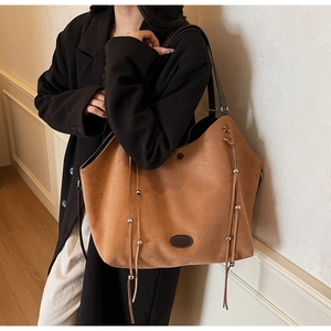 Detail of large brown suede tote bag with fringe accents and metallic bead charms