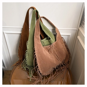 Detail of three suede hobo tote bags in green, brown and beige with long fringe accents