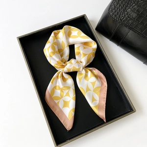 Detailed close-up of yellow silk scarf with geometric pattern in a black display tray