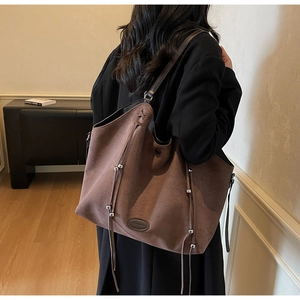 Détail d'un grand sac cabas en daim marron avec des franges et des perles en métal