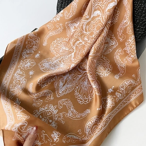 Foulard en soie marron doré à motif paisley drapé sur un sac en cuir noir élégant