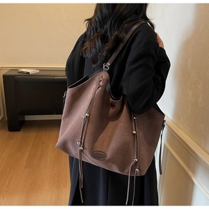 Détail du grand sac cabas en daim marron avec pampilles et logo embossé porté à l'épaule