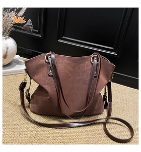 Detailed view of brown suede tote bag with bronze hardware on a textured woven rug