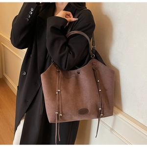 Détail d'un cabas en daim marron avec pompons porté sur une veste de costume noire
