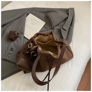 Top view of brown suede bucket bag with leather strap on stylish blazer background