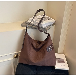 Detail of suede tote bag showing side leather zipper patch and silver rivet accents