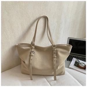 Detail of minimalist cream tote bag showing leather strap and metal eyelet accents