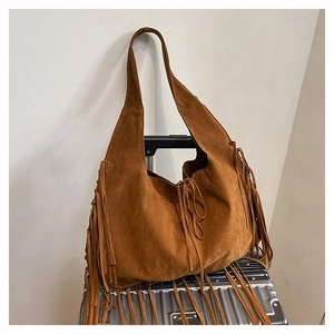 Detail of a brown suede tote bag with long fringes and decorative laces on a suitcase