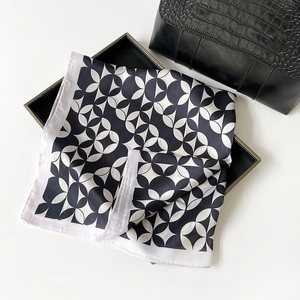 Elegant satin scarf with black and white geometric pattern next to a black leather handbag
